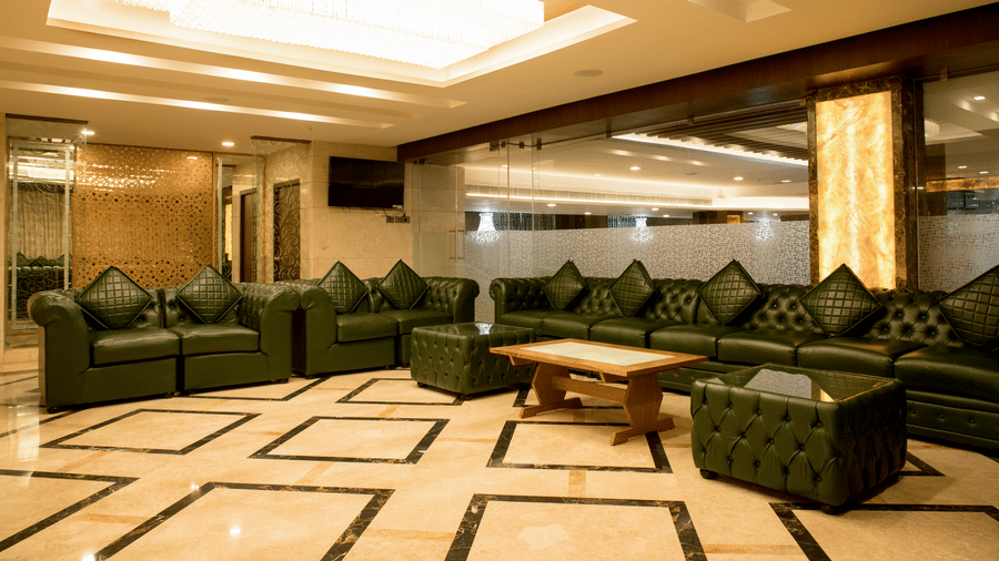 A spacious lounge area at Benzz Park Chennai with dark green sofas and a patterned floor, ideal for relaxation.
