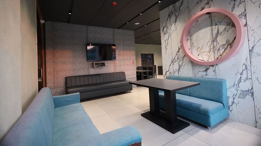 The image shows a modern lounge area with sofas, a table, a television, and a circular mirror on a patterned wall - Lords Eco Inn Navsari.