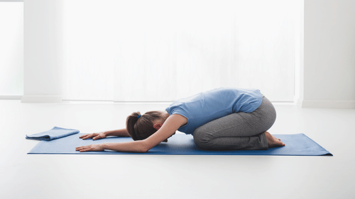 A person performs the Child's Pose on a yoga mat indoors