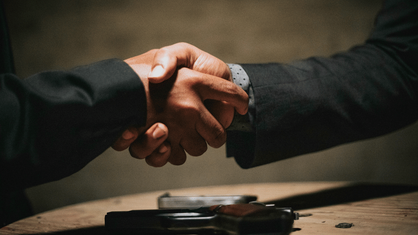 A close-up of two people in dark suits shaking hands over a table | HHI Varanasi
