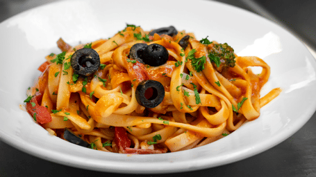 Plate of tagliatelle pasta topped with olives and vegetables.