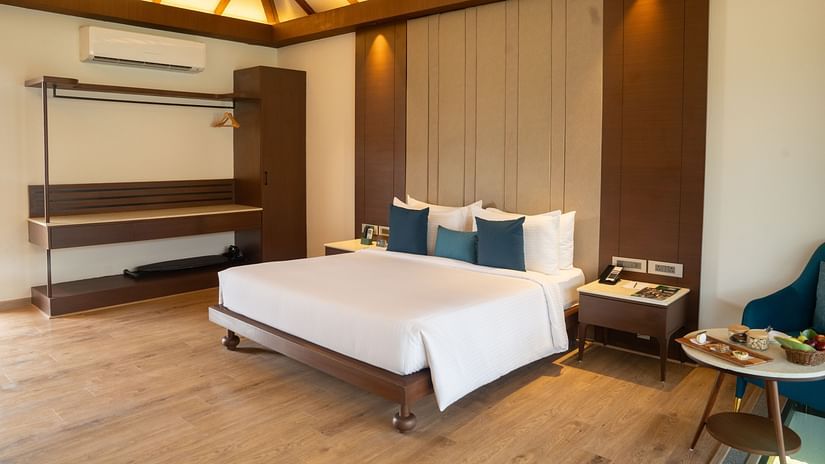 A King-size bed room with ceiling fan, wall-mounted air conditioner, sitting area, storage unit, and bed-side table at Ananta Spa and Resort, Ajabgarh.