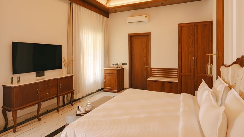 A hotel room with a bed, a television on a dresser, and a doorway leading to another area.