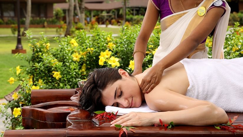 A woman lying on her stomach outdoor received a massage on her neck and shoulders at Ayuveda Spa, Uday Backwater Resort