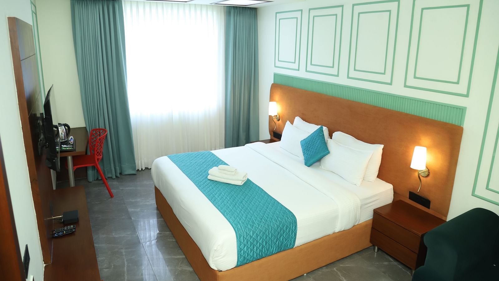 A comfortable room includes a double bed with a turquoise accent and wooden furniture - Asian Suites IFFCO Metro, Gurgaon
