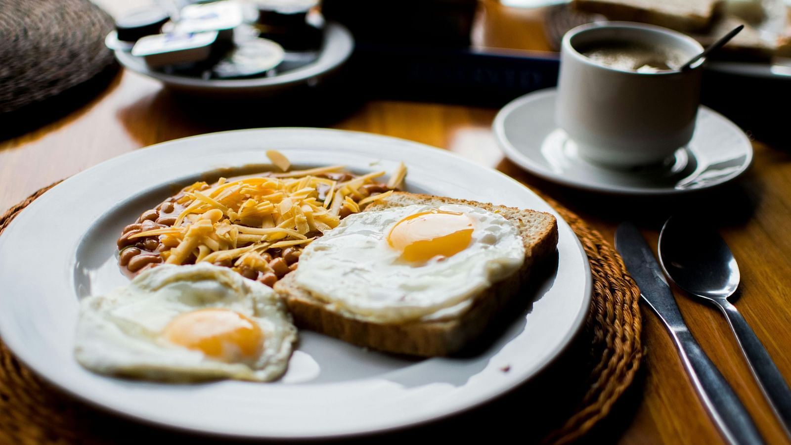 A breakfast plate with two fried eggs, beans topped with grated cheese, and a slice of toast.