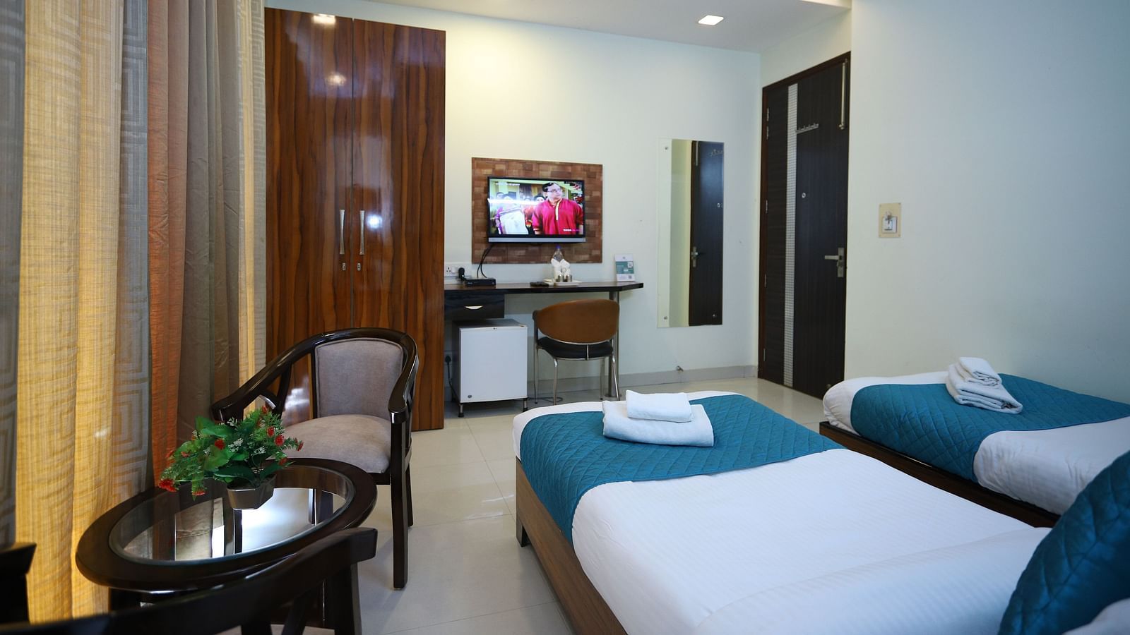 A room with two single beds and a seating area, featuring warm lighting and a mirror on the wall - Asian Suites Cyber Park, Gurgaon