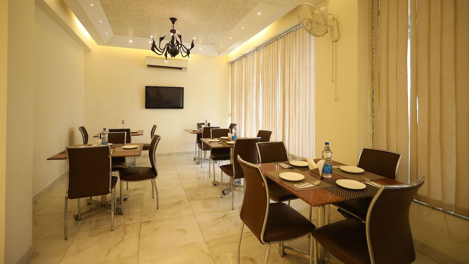 A well-lit dining space with several tables and chairs is decorated with sheer curtains and a chandelier - Asian Suites Cyber Park, Gurgaon