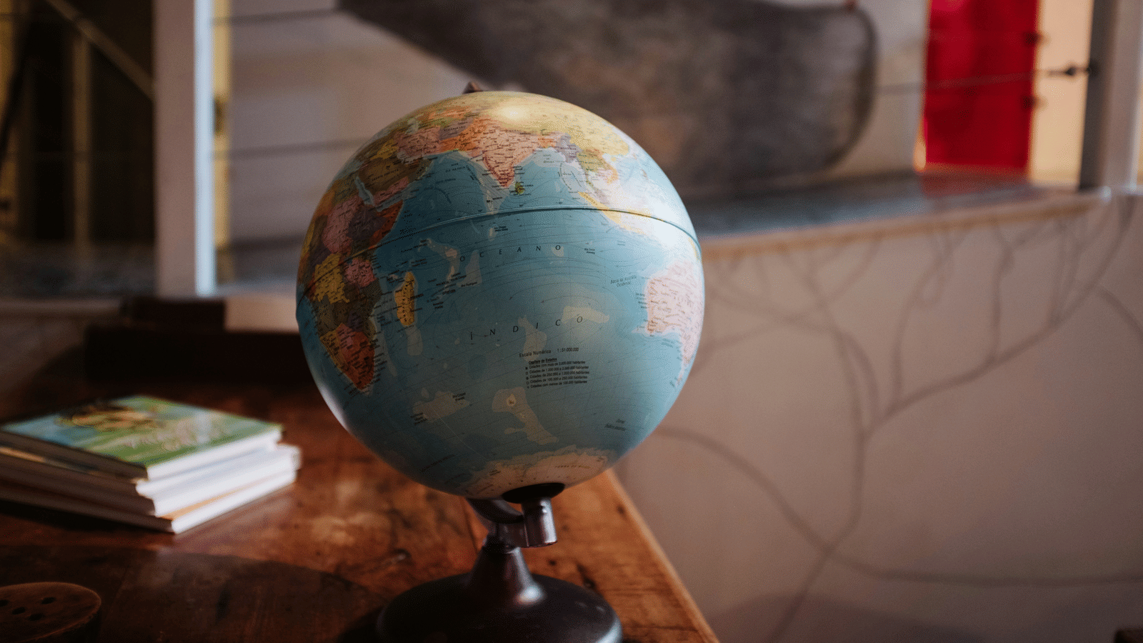 A globe kept on a table with books behind it.