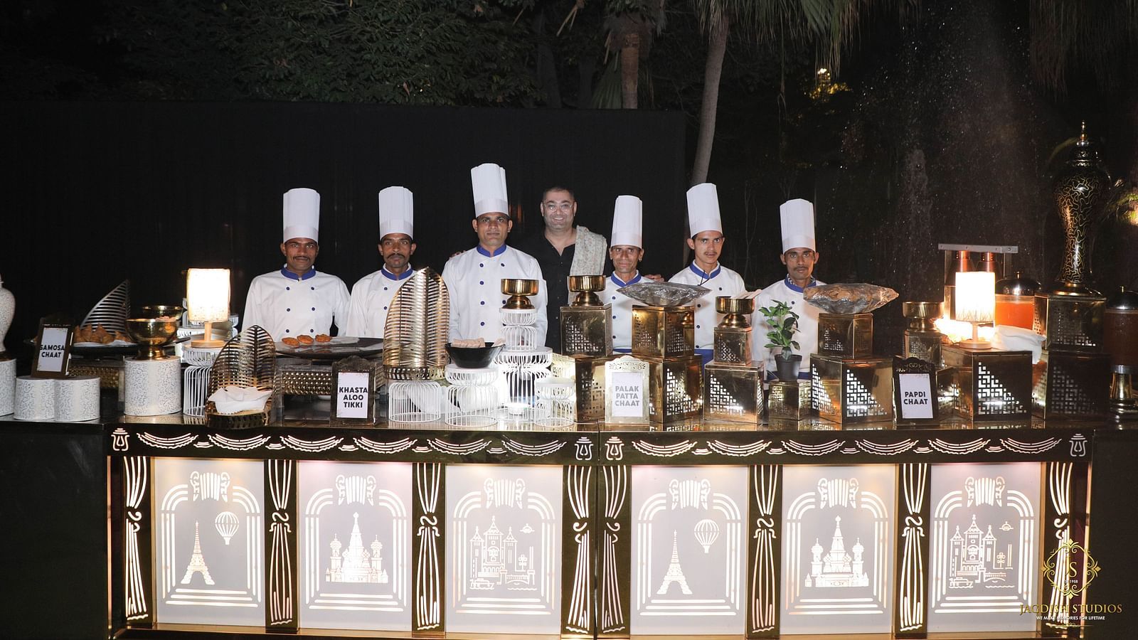 Chefs presenting dishes at the buffet counter under the night sky, with open-top dining set up at the 'Around The World in Eighty Plates' event.