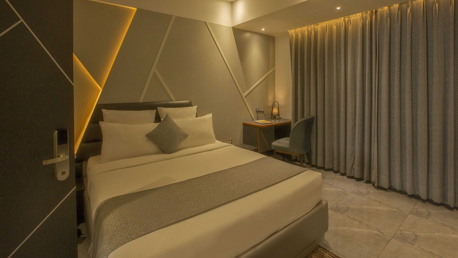 Image of well lit Coral Premium Room at Coral Reef Hotel and Spa in Port Blair featuring a plush bed and a work desk and chair next to it near the window