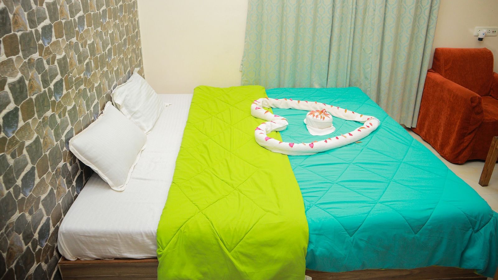 side view of the king size bed with a teal and green coloured comforter spread over it with pastel coloured curtains in the far end of the room