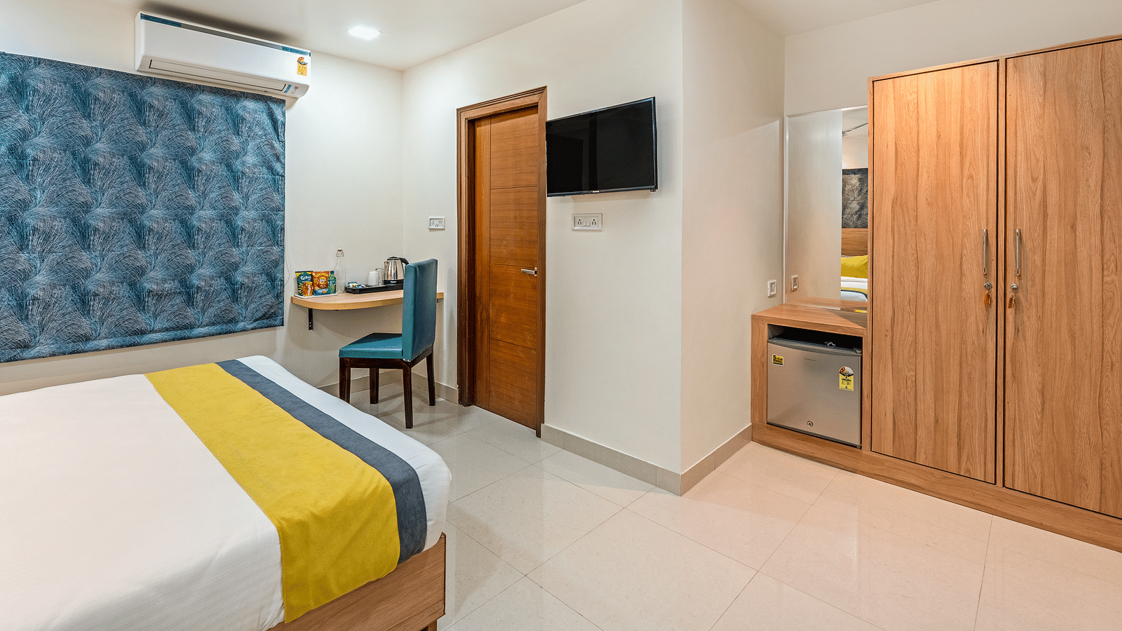  A wide angle shot of a bed in a room at the hotel featuring a flat screen television, a study table, chair, wooden cupboard | Eminent Suites & Apartments, Hi-Tech City