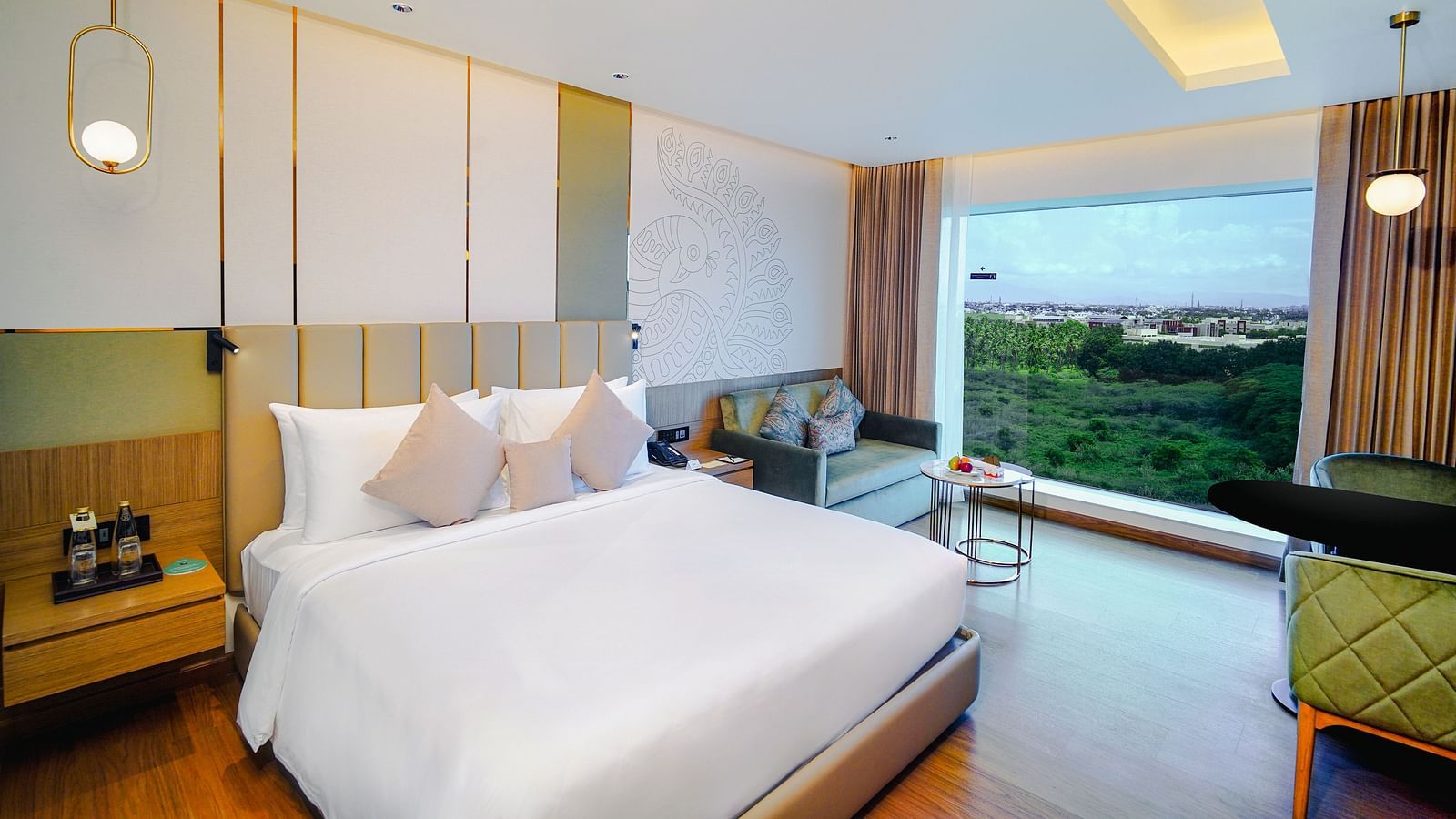 A bright, modern hotel room with a large bed, a comfortable sofa, and a wide window offering a view of lush greenery - Grand Madurai by GRT Hotels
