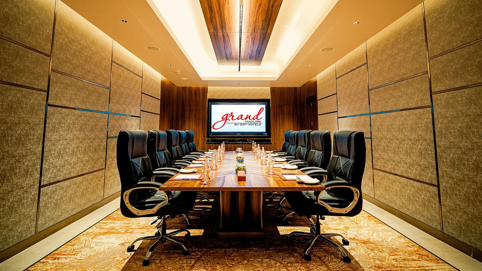 A modern conference room with a large table, executive chairs, and a presentation screen - Grand Madurai by GRT Hotels