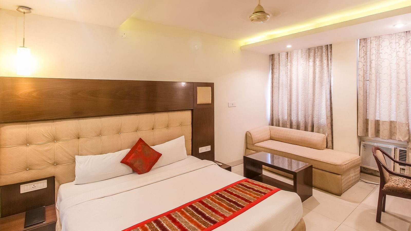 A cosy hotel room with a plush bed, a small sofa, and a glass-topped table. - Hotel Diamond Plaza, Chandigarh.