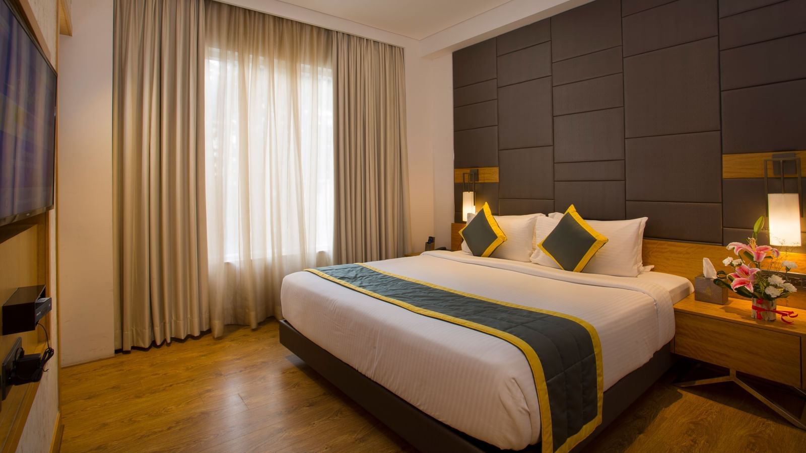 a bedroom with a large bed opposite a television mounted on the wall and side drawers on each side - Hotel Fountain Tree By TGI - JP Nagar, Bangalore