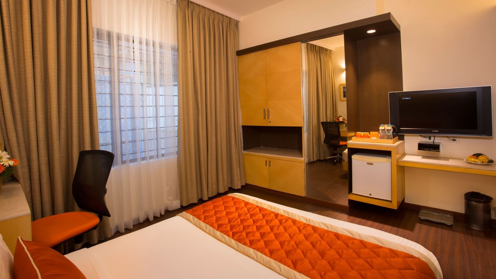 An inviting hotel room with a large window covered by sheer and opaque curtains, a wooden wardrobe and a flat-screen TV - Hotel Langford Keys by TGI, Shanti Nagar