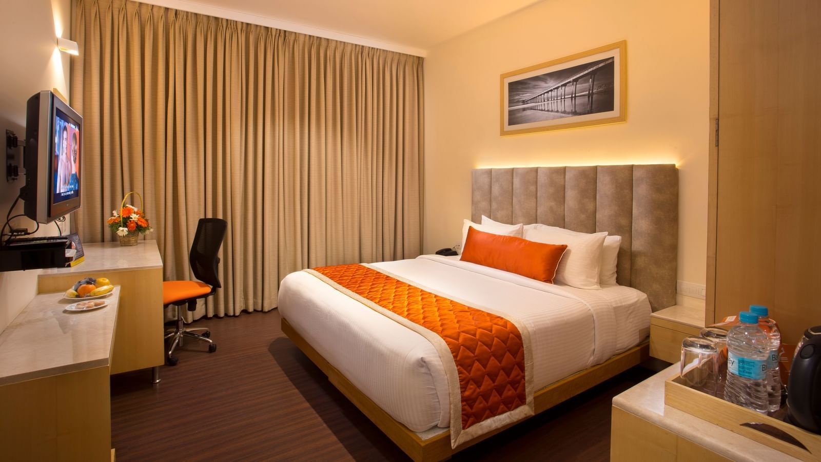 A cosy hotel room with a plush bed adorned with an orange bed runner, a work desk and a wall-mounted TV - Hotel Langford Keys by TGI, Shanti Nagar