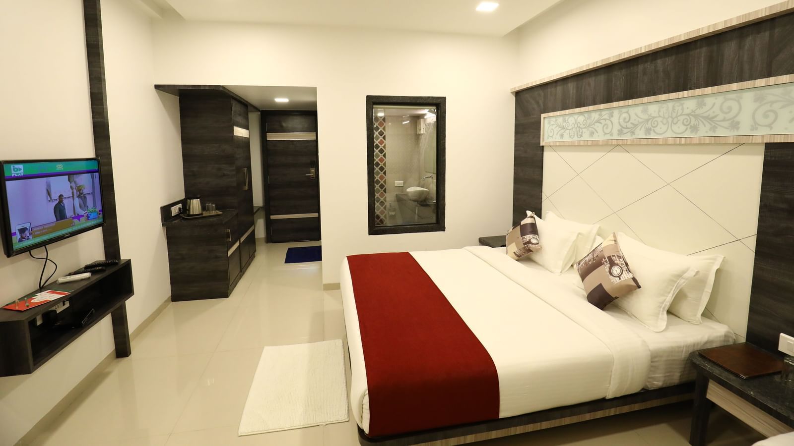 A room in Imperial Grande with a bed covered in white and red bedding, a television on a stand, and a mirror on the wall.