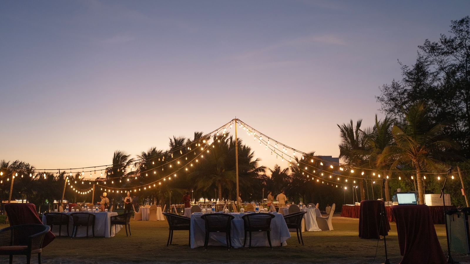 Outdoor evening event setup with string lights and a sunset backdrop - Kaldan Samudra Palace