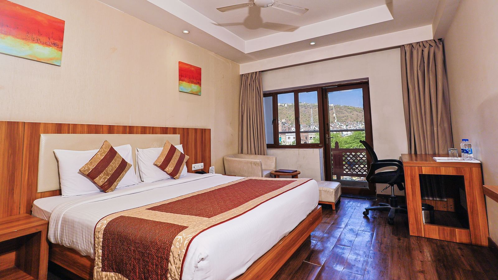 A low angle view of the bedroom with comfy bed and balcony, table and fan at Le Roi Udaipur