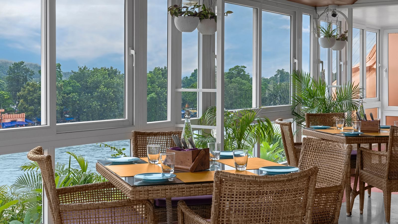 Indoor seating at The Patio café in Ganga Lahari, Haridwar with large windows offering serene views of the Ganges and lush greenery.