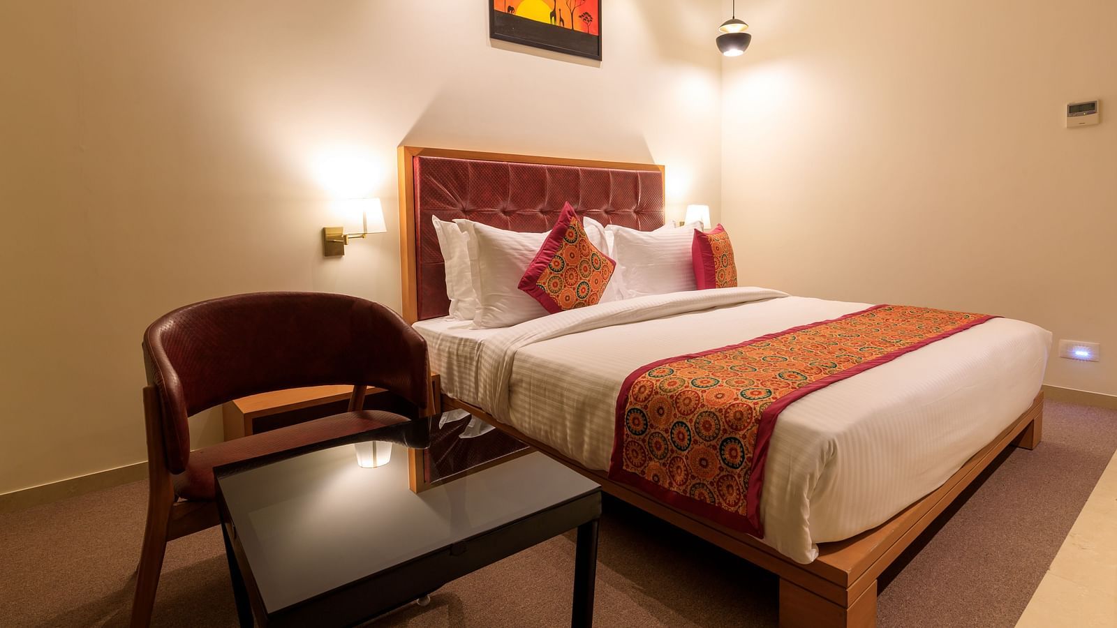 A warmly lit hotel room at Lords Eco Inn Apple Gate features a double bed with patterned accents, a chair and a small table.