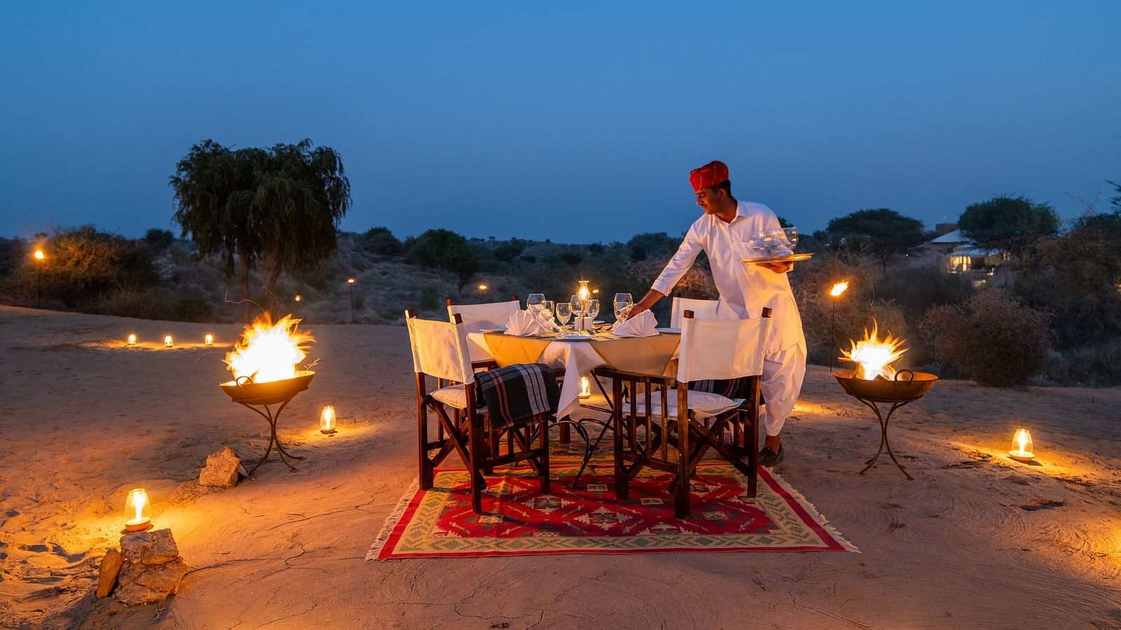 A man making an arrangement for the dinner in an outdoor setting with is decorated with lights - MANVAR Resort & Desert Camp