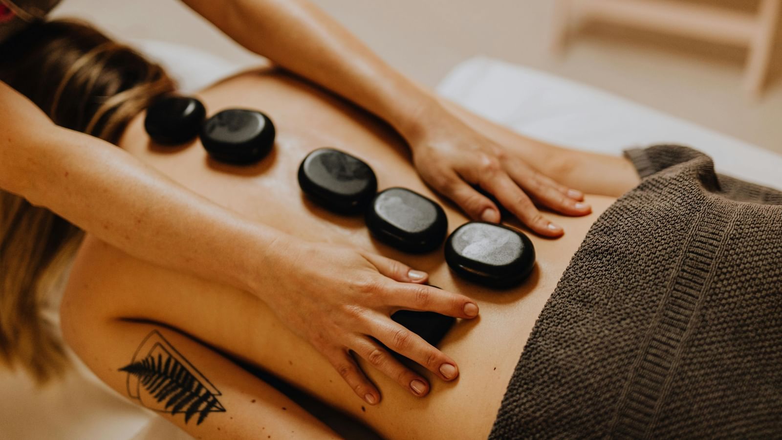 A therapist performing a hot stone massage on a patient's back, gently placing the heated stones along the spine.