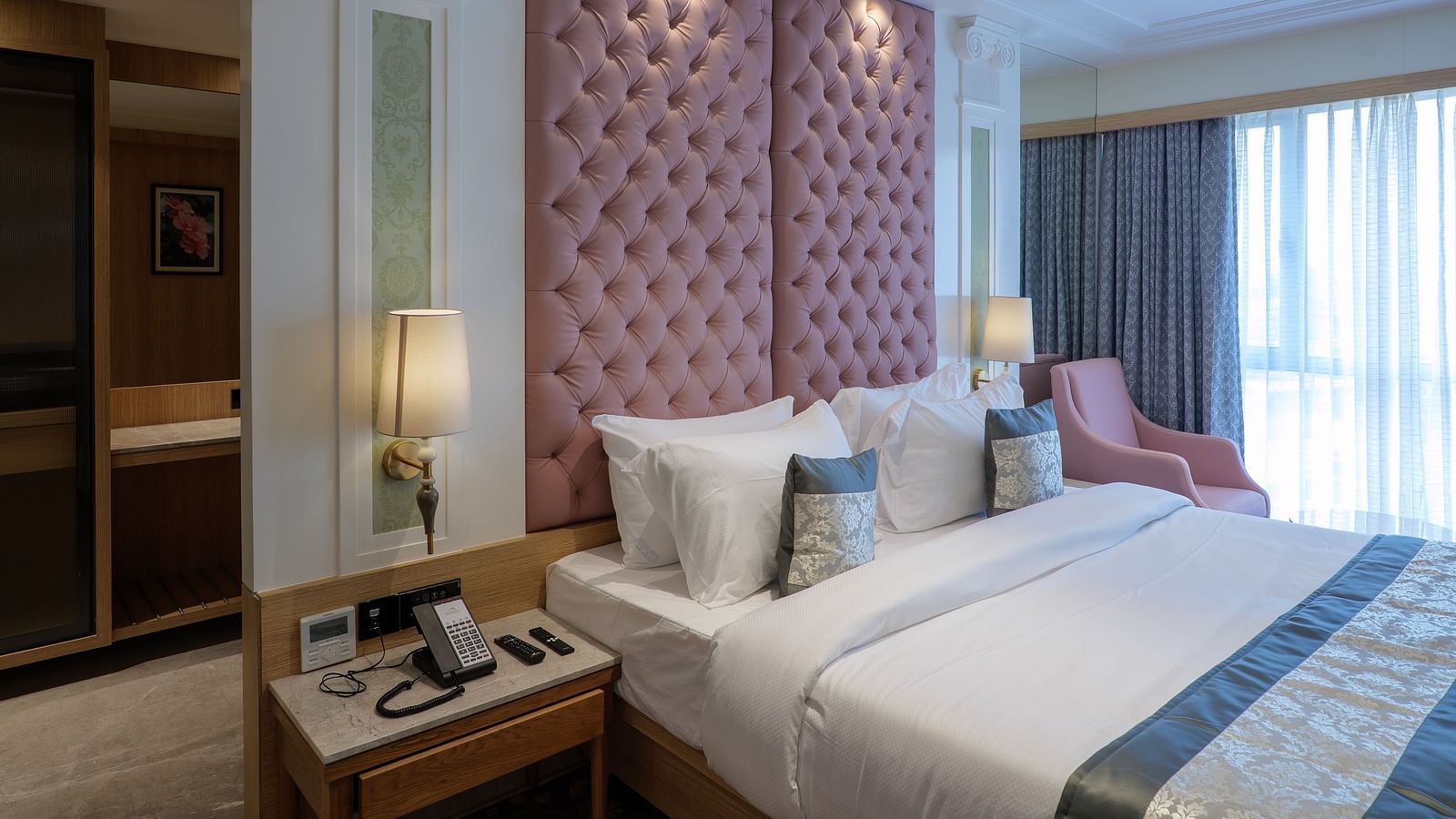 A room with a large bed featuring a pink tufted headboard, bedside tables, and an armchair with soft lighting - Melior Inn