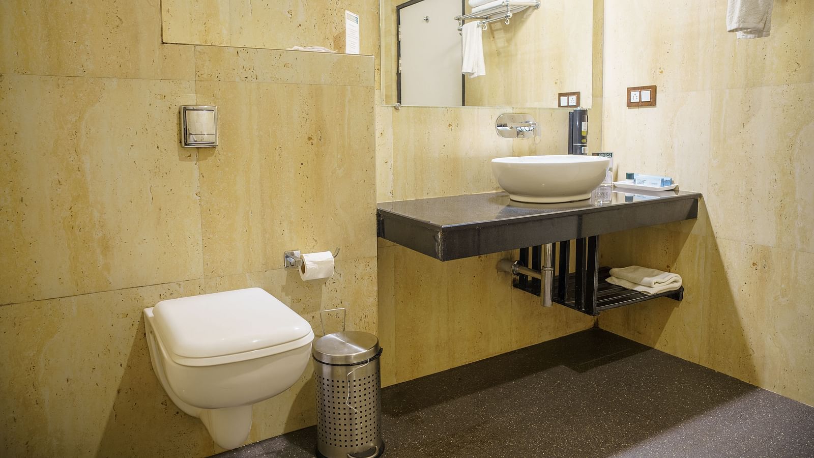 A modern bathroom at Orsino Spa Resort with a toilet, a basin set into a vanity, and light-coloured tiled walls.
