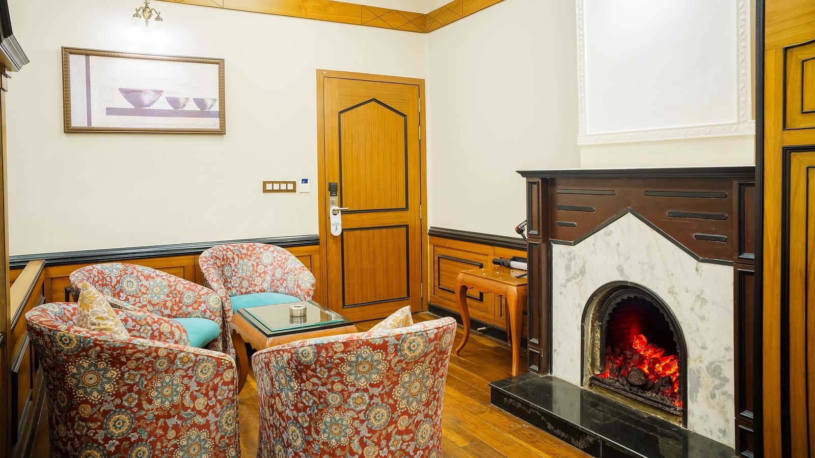 A seating area at Orsino Spa Resort with patterned armchairs and a sofa, a fireplace with a lit fire, and wooden wall panelling.