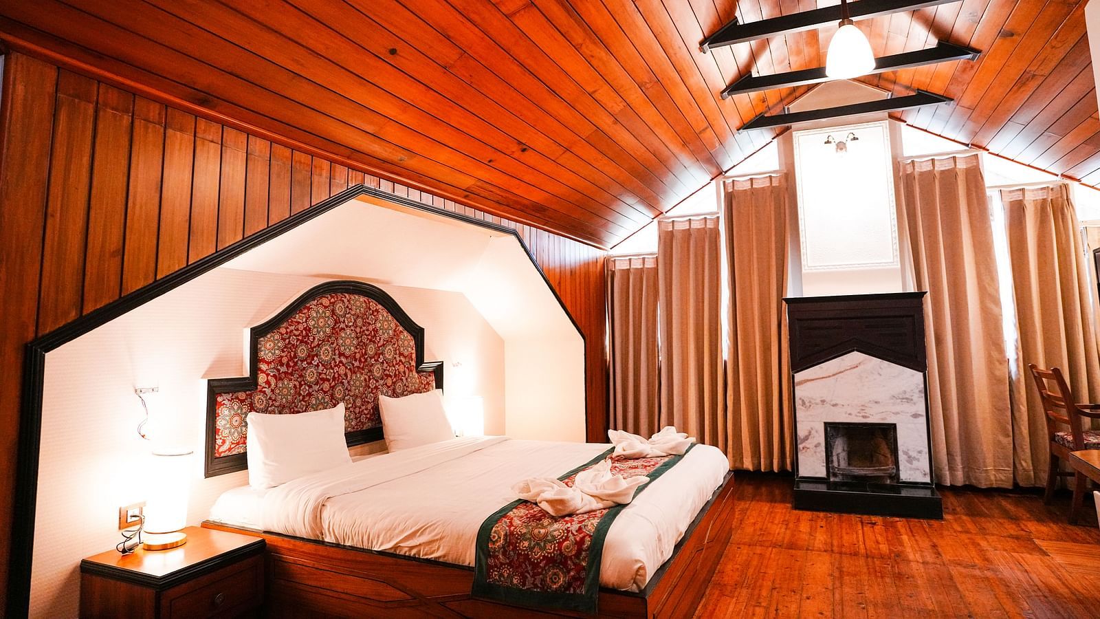 A room at Orsino Spa Resort with a wooden ceiling, featuring a bed with white linen and a red bed runner, and wooden panelling.