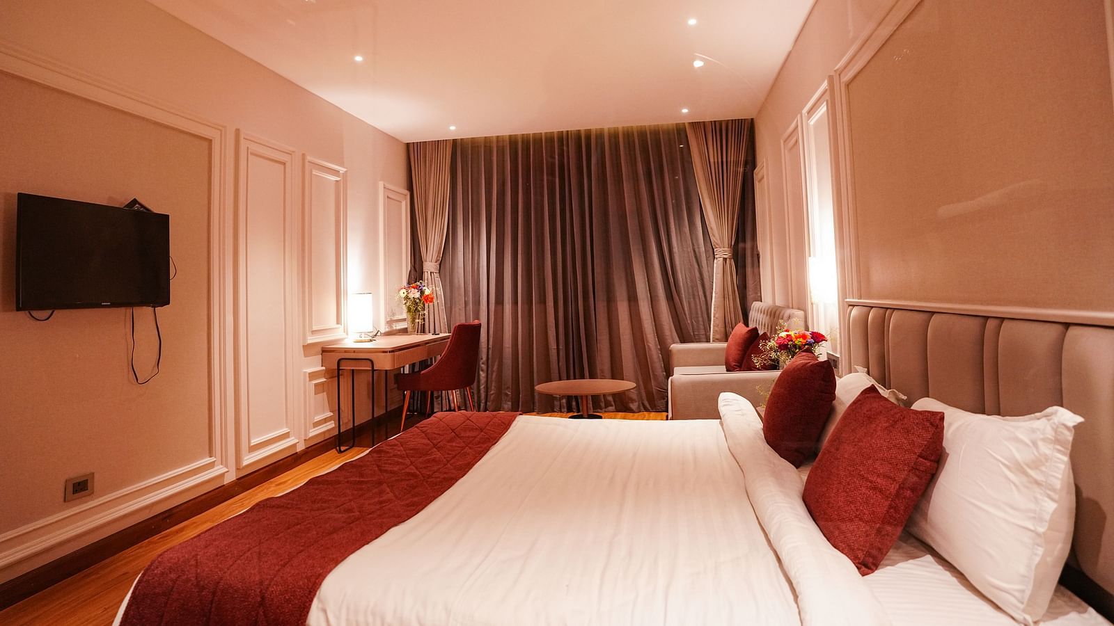 A room at Orsino Spa Resort with a large bed dressed in white linen and a red bed runner, with curtains and warm lighting.