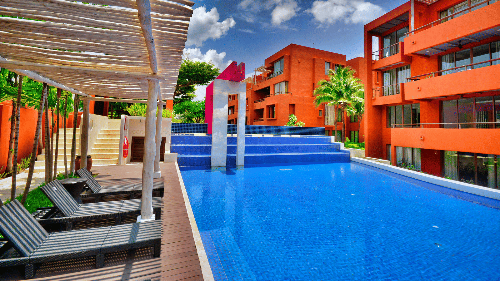 Vibrant hotel facade featuring sun loungers and a pool.