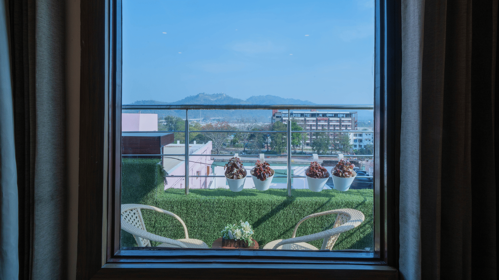 View from a hotel window overlooking a green outdoor terrace area and distant landscape - Perfectstayz Premium at Har Ki Pauri Road (Ganga Heights)