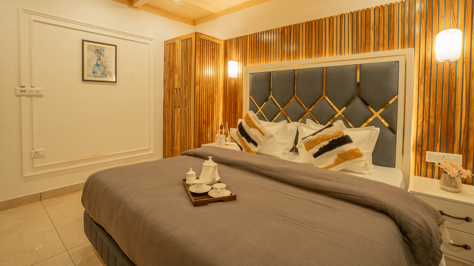 A bedroom with a king size bed, a tray with cups and a kettle, wall-mounted lights, and a bedside table at Perfectstayz Value Paradise, Mussoorie.