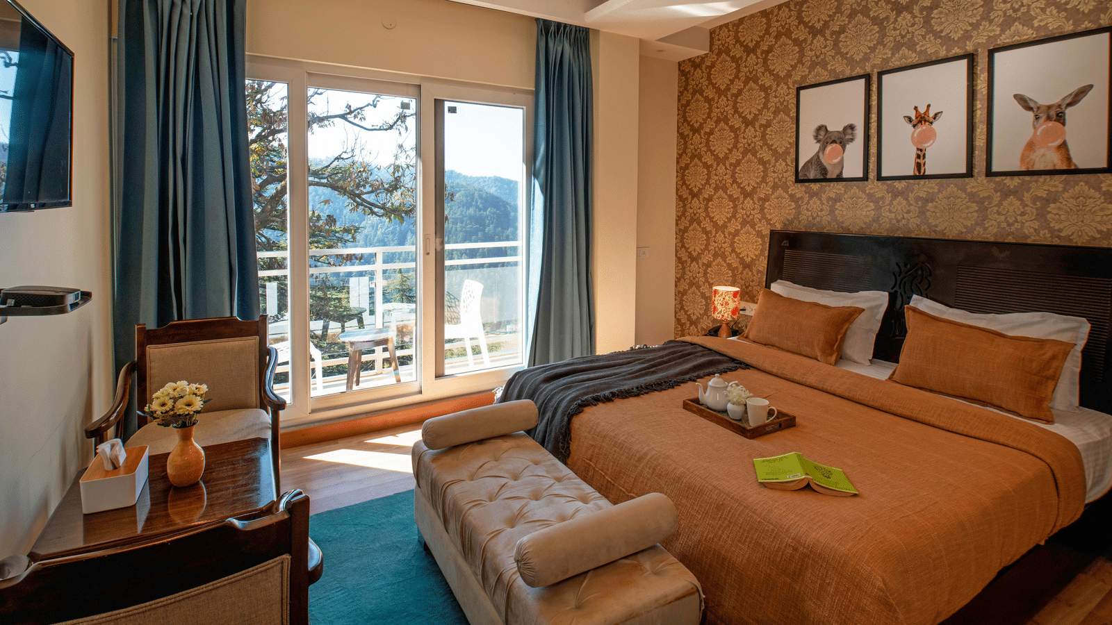 A bedroom at Perfectstayz Value Shimla (Namah Retreat) with a king size bed, wall art, a television, a table, 2 chairs, a daybed, a tray with cups and a kettle, and a sliding door leading to a balcony with a table and chairs.