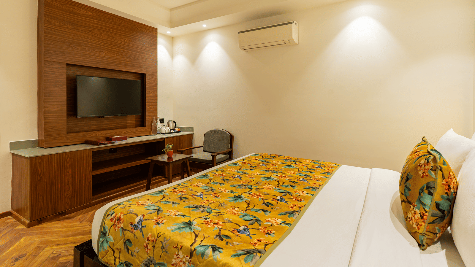 A bedroom featuring a bed, an A/C unit, a television unit, and a chair and a small wooden table | Summit by the Ganges Beach Resort & Spa, Rishikesh