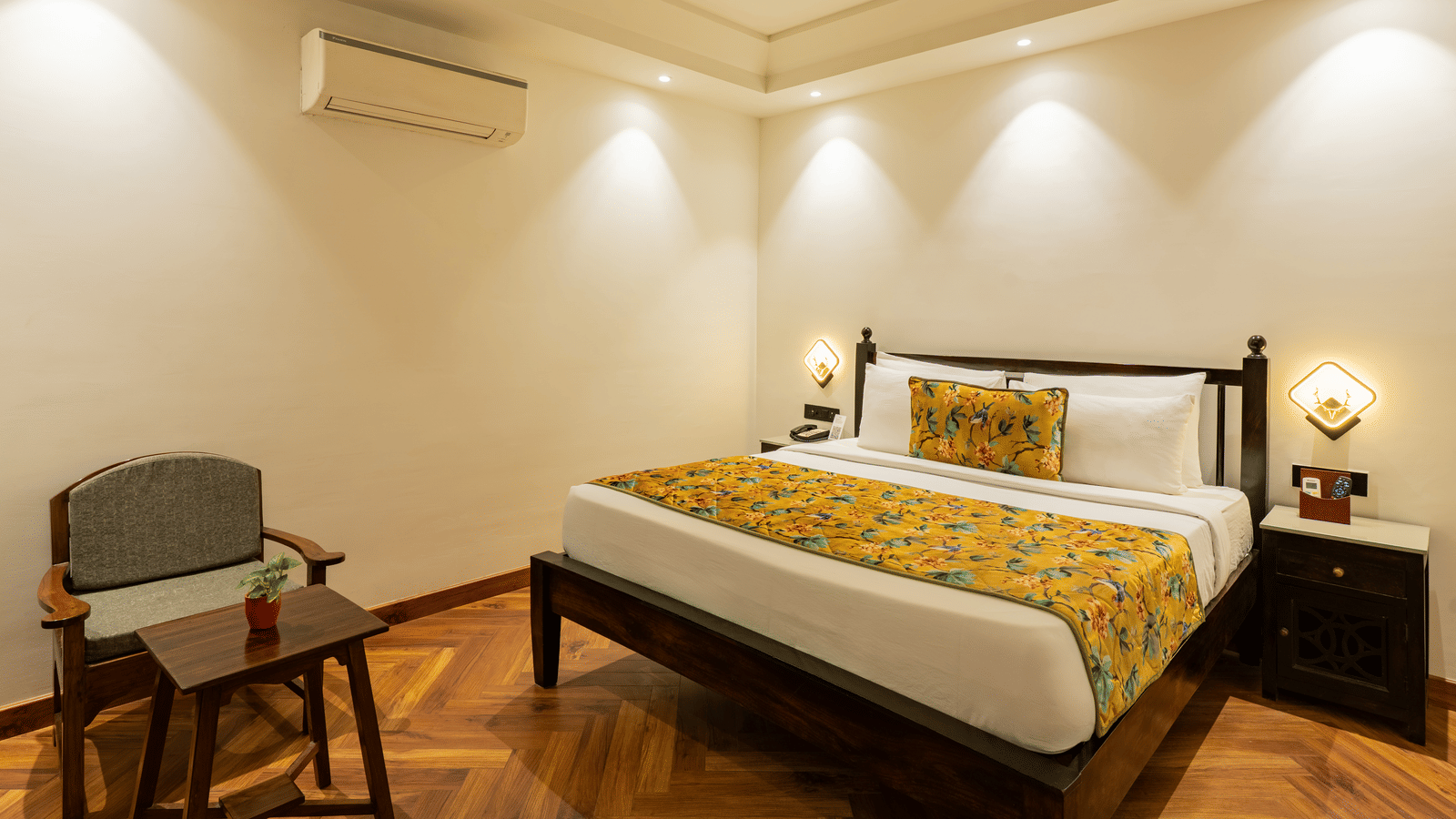 A bedroom featuring a wooden bed with a bedside cabinet, an A/C unit, and a small table with a chair | Summit by the Ganges Beach Resort & Spa, Rishikesh