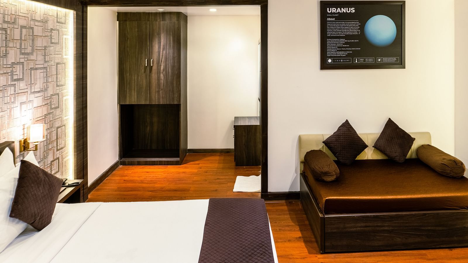 Hotel room corner with a cushioned brown daybed, decorative pillows, a wardrobe, and a framed Uranus information poster on the wall - The Grand Legacy Resort & Spa