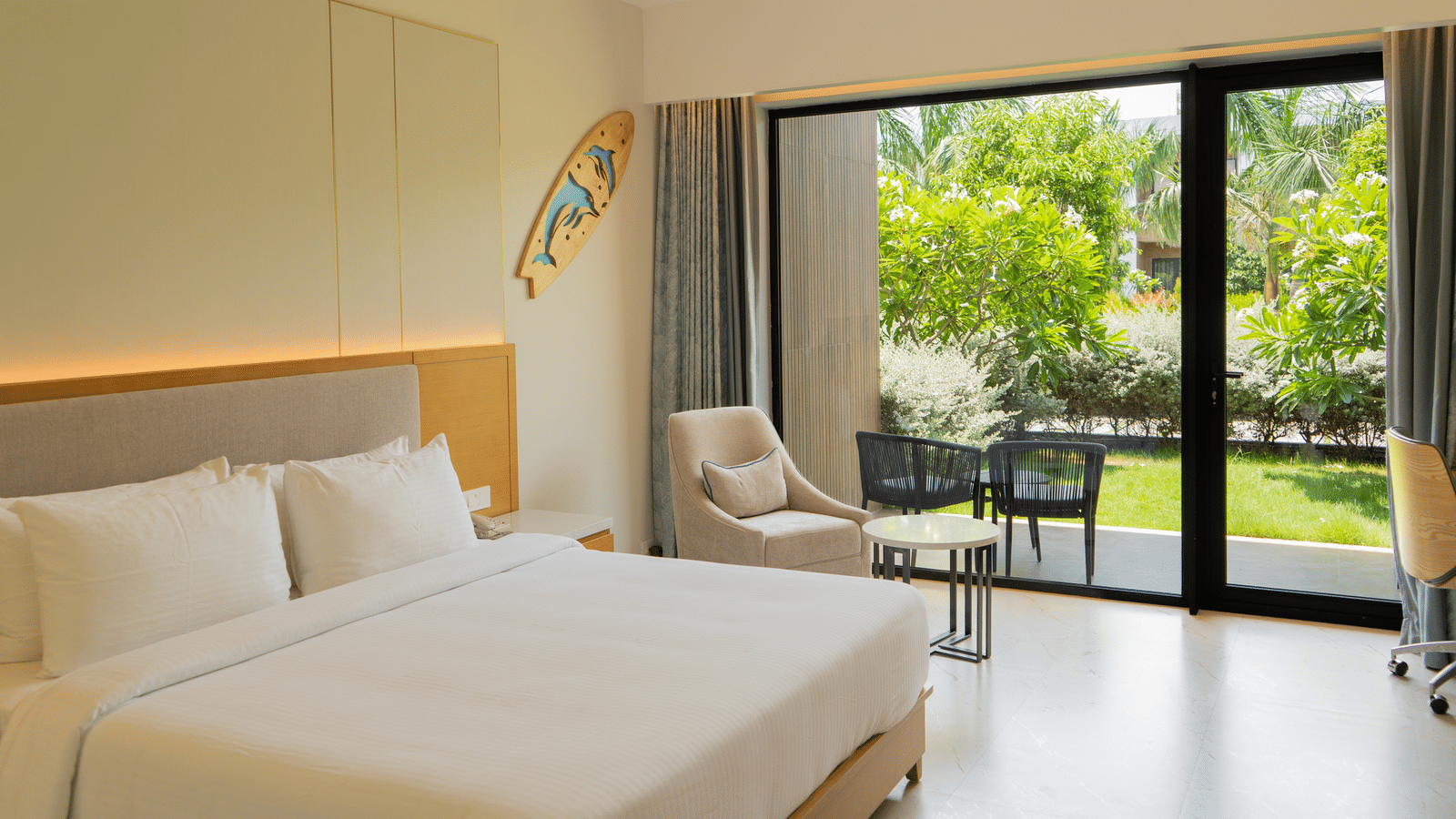Garden Courtyard room at The Shore Trishvam, Pondicherry, with floor-to-ceiling glass doors opening to a lush tropical garden and outdoor seating.