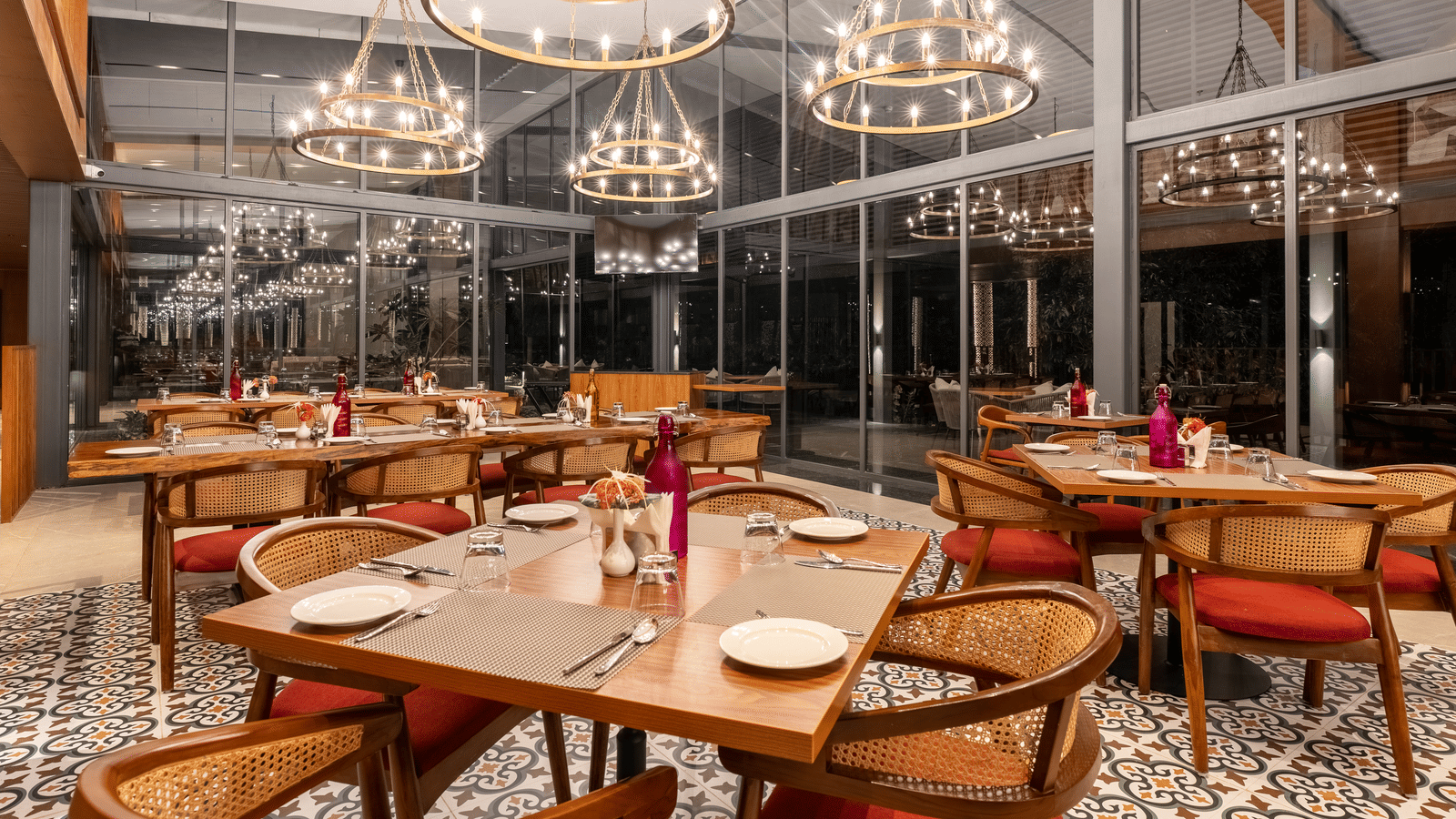 A  stylish restaurant setting at Wyndham Garden with round tables, modern lighting, glass facade interior, dark wood tables, and  circular chandeliers. 