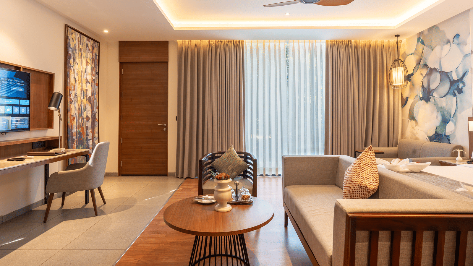 The living area of a guest room at Wyndham Garden with a  multi-seating sofa, a round table, a flat-screen television, and large glass windows