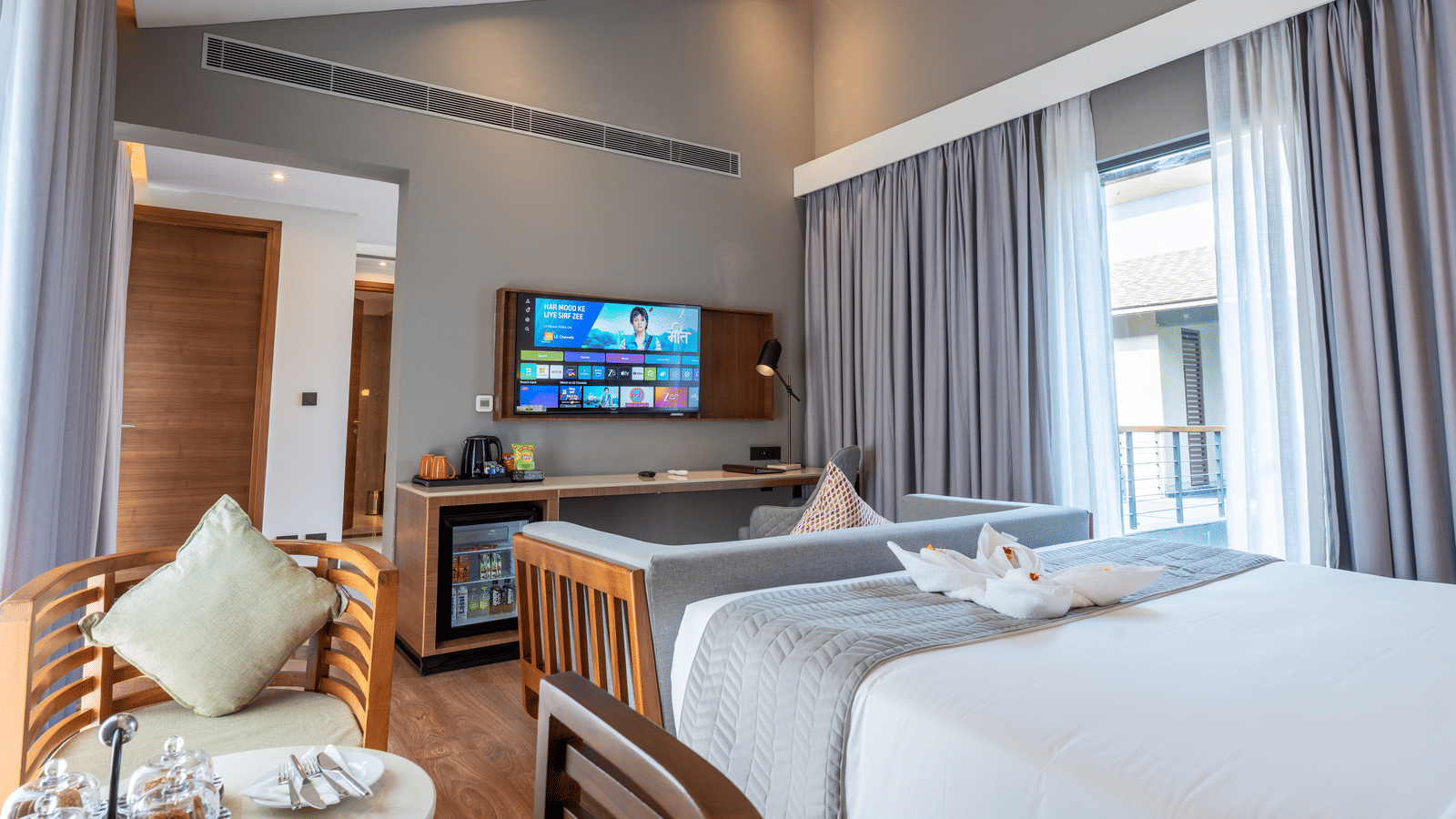 A Wyndham Garden bedroom with 2 separate beds, a mounted TV, and a window dressed with floor-length curtains.