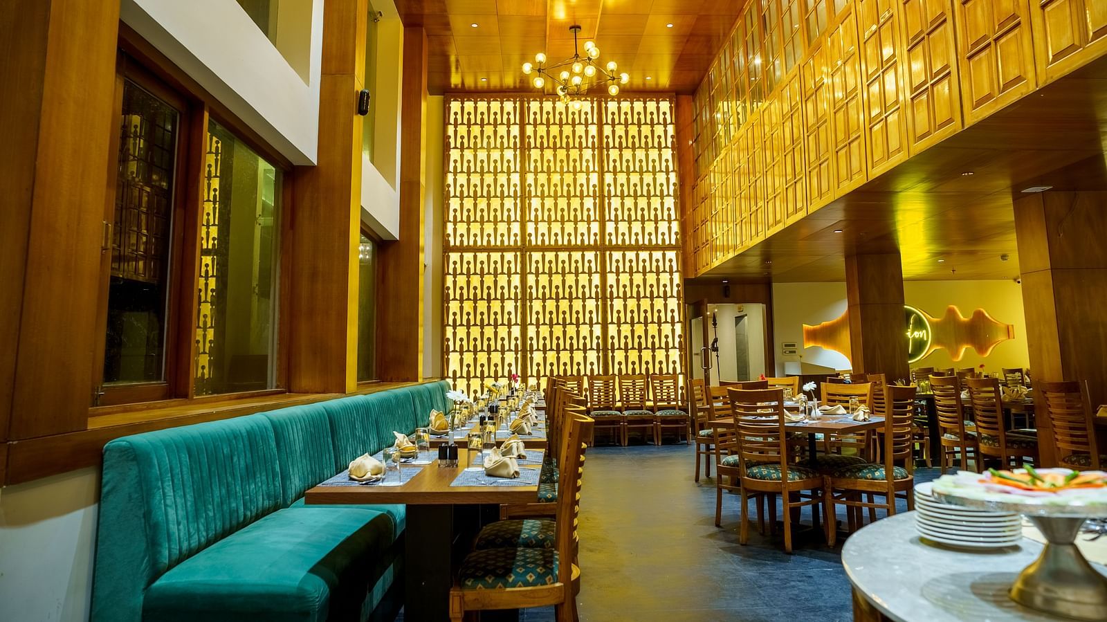 A warmly lit restaurant at Orsino Hotel & Spa features wooden walls, varied seating including a teal banquette, and set tables.