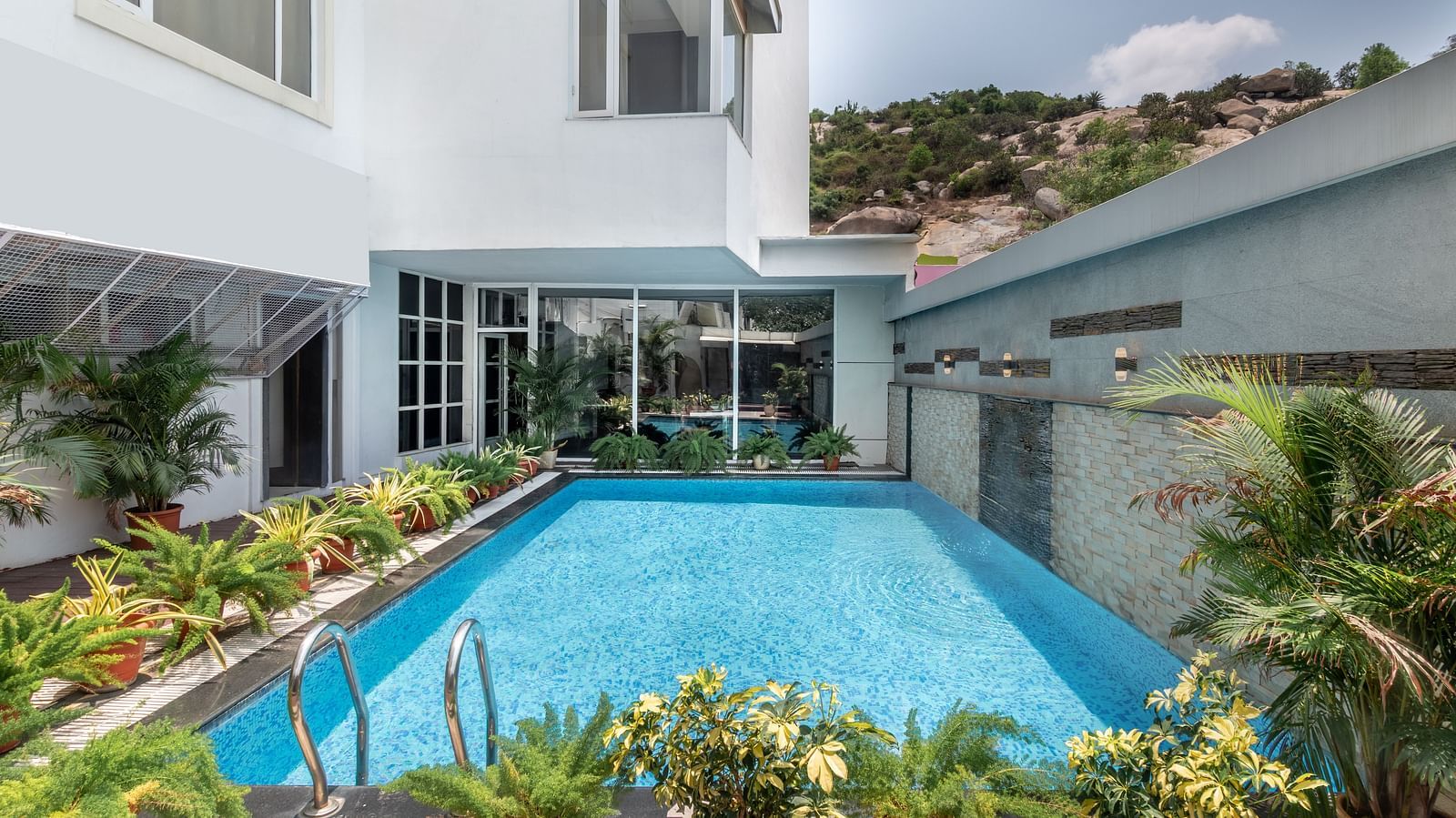 A swimming pool with clear water is surrounded by landscaping and a white building. The sky is overcast.