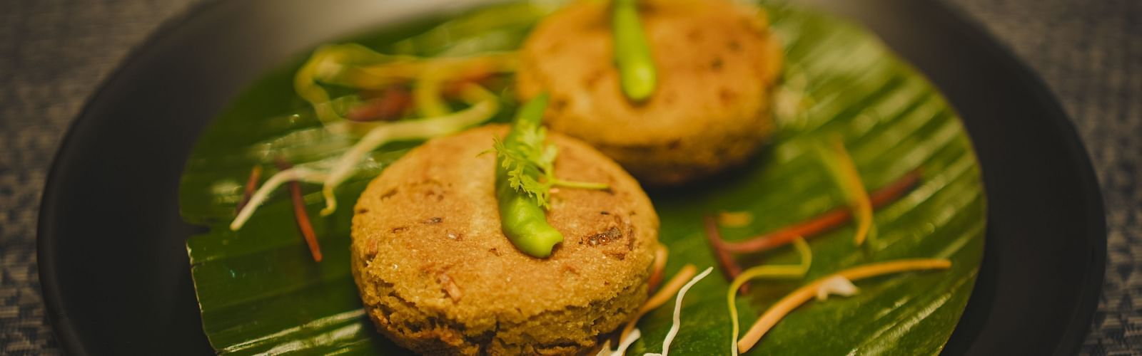 image of a two cutlets placed over a banana leaf topped with green chillies - Dip Holidays, Birbhum