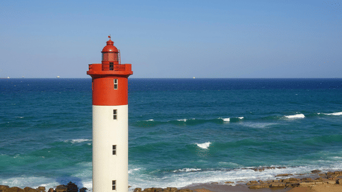 A view of a lighthouse near the Best Beach in Kovalam with a clear sky in the background where waves can be seen hitting the shore